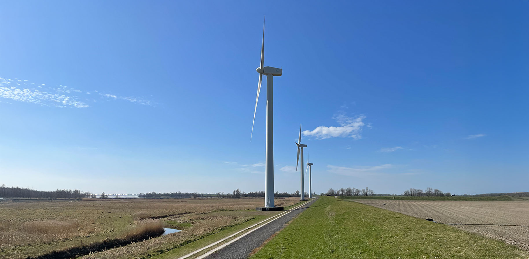 De afbeelding toont drie windturbines langs een pad tegen een heldere blauwe lucht.