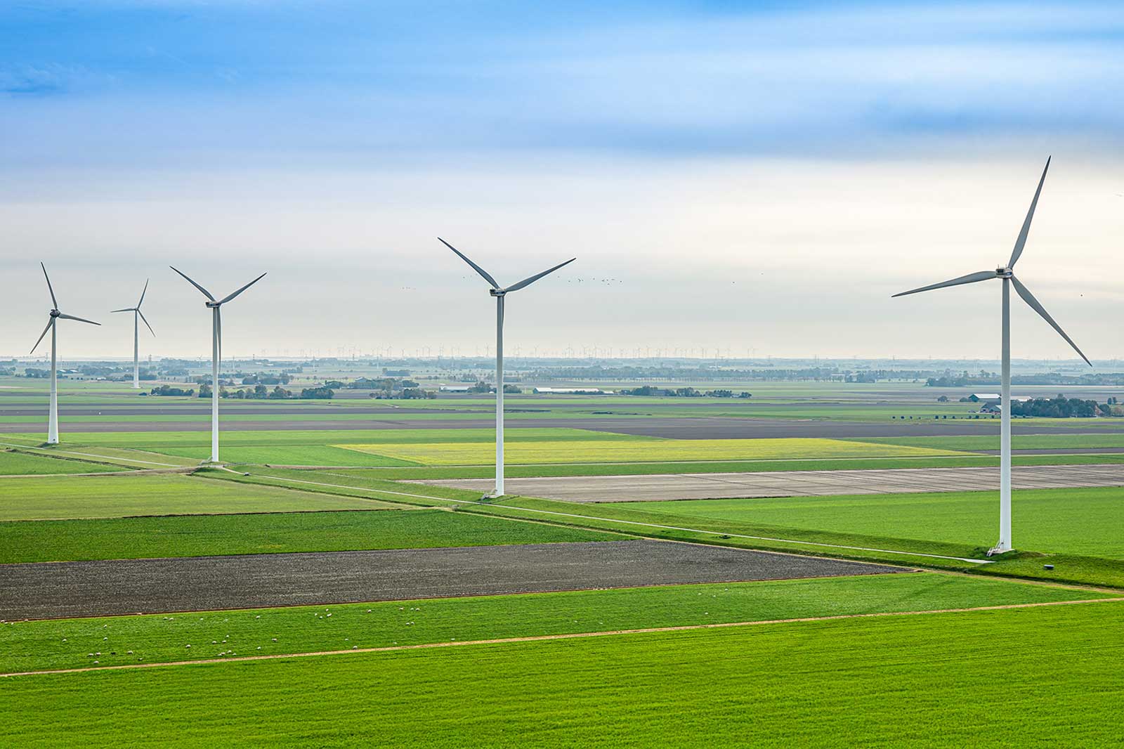 Een schilderachtig uitzicht op verschillende windturbines in groene velden onder een bewolkte lucht, die duurzame energie tonen.