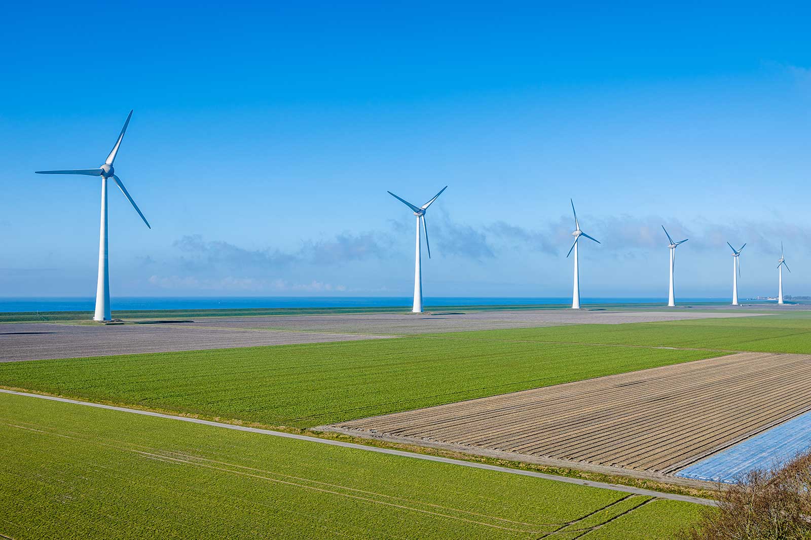 Een landschap met meerdere windturbines tegen een heldere blauwe lucht, met uitzicht op groene velden en de verre zee.